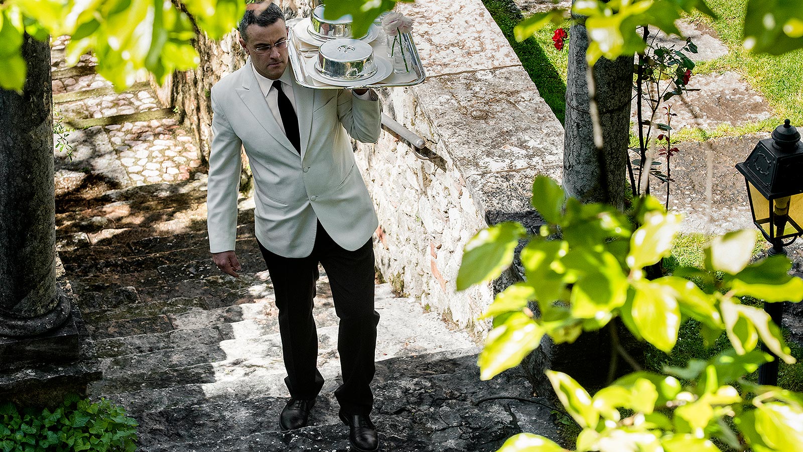 Un serveur monte les escaliers du jardin avec un plateau et de la nourriture